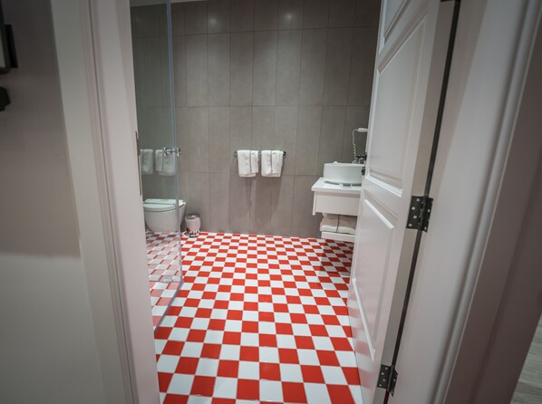 Un baño con piso a cuadros rojo y blanco, un lavamanos blanco y un inodoro.