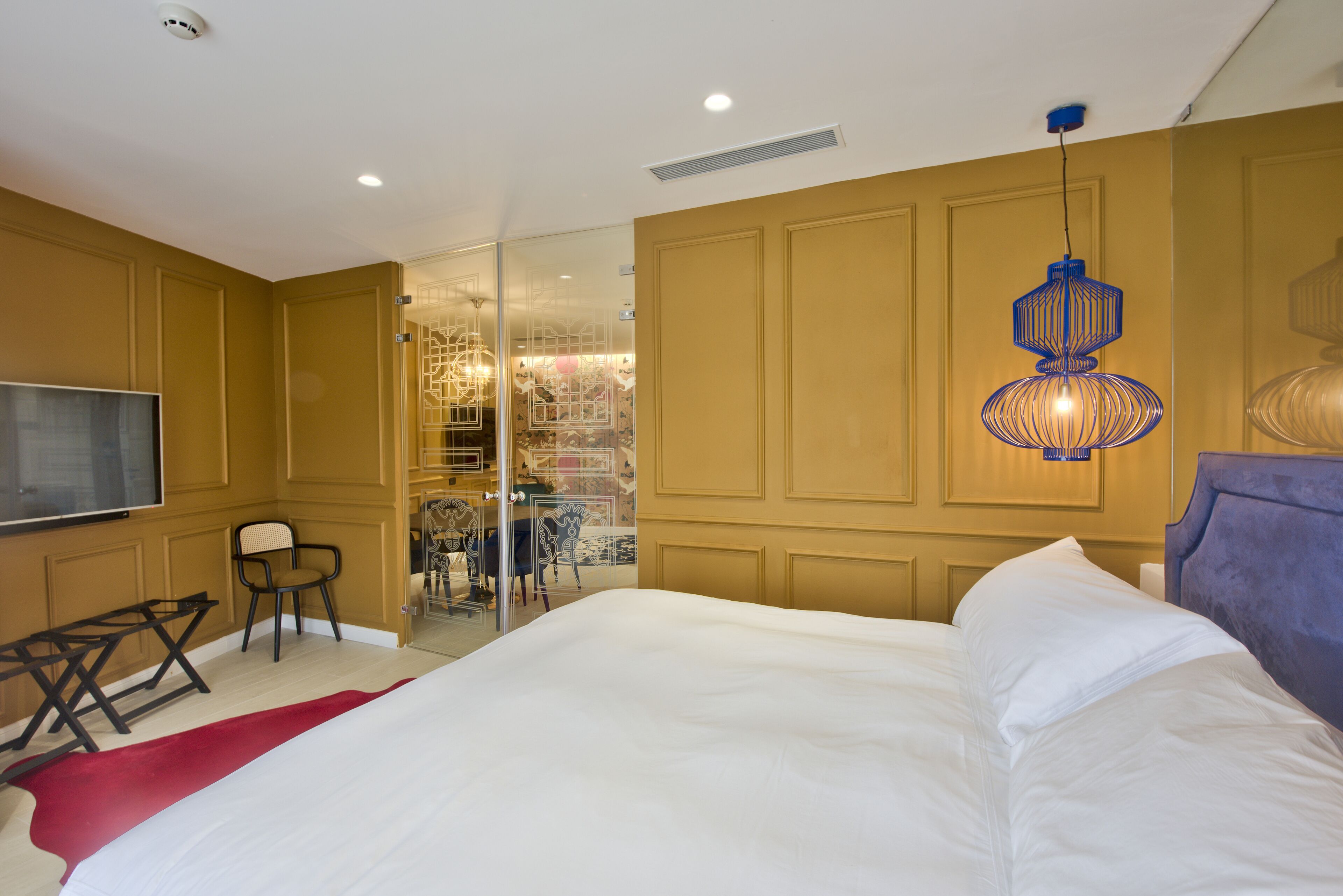 A bedroom with a large bed, a TV, a chair, and a hanging light fixture.