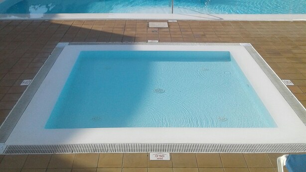 Una piscina con borde de baldosas, un flotador salvavidas y un cartel que indica la profundidad.