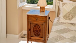 Un dormitorio con vista al mar, una mesita de noche de madera con lámpara y una cama con colcha.