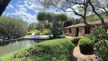 Une maison en pierre avec un toit en tuiles, une piscine et une terrasse en bois équipée de chaises longues.