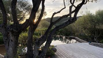 Une terrasse en bois donnant sur une étendue d’eau, avec des arbres et des collines en arrière-plan.