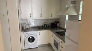 Una cocina compacta con armarios blancos, lavadora, microondas, fregadero y estufa.