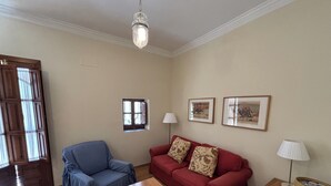 Una sala de estar con un sillón azul, un sofá rojo, una mesa de madera y una lámpara colgante.