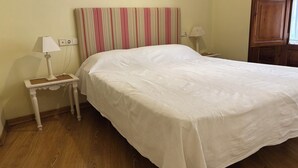 Una cama bien tendida con un cabecero a rayas, una mesita de noche con una lámpara y suelo de madera.