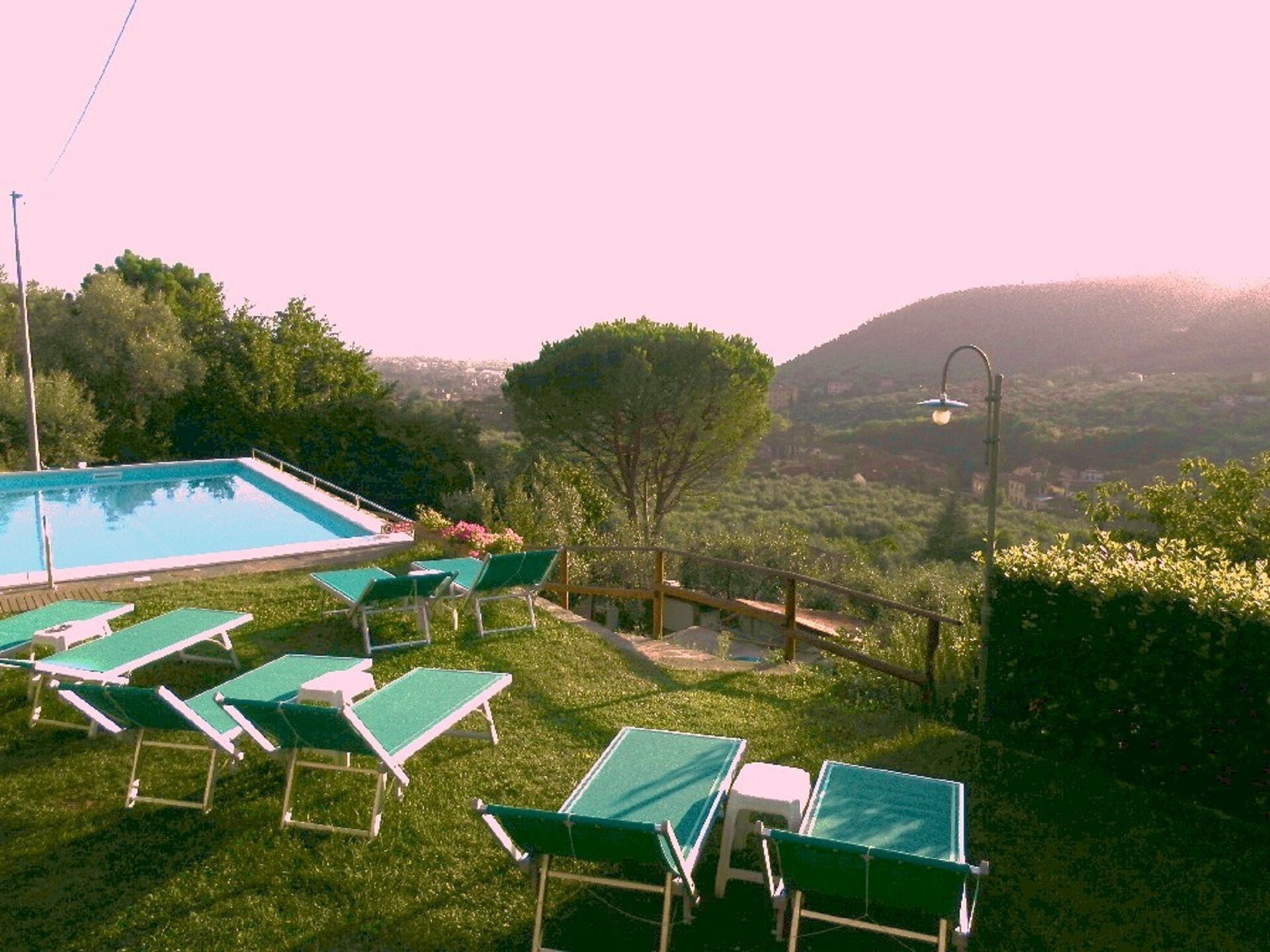 A pool area with green lounge chairs and a view of a hilly landscape.