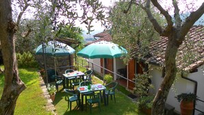 An outdoor patio with a stone wall, green chairs, a table set with plates and a bottle, and two green umbrellas. - PROMOTION Typical Tuscan dwelling, house with garden among olive trees (Calci)