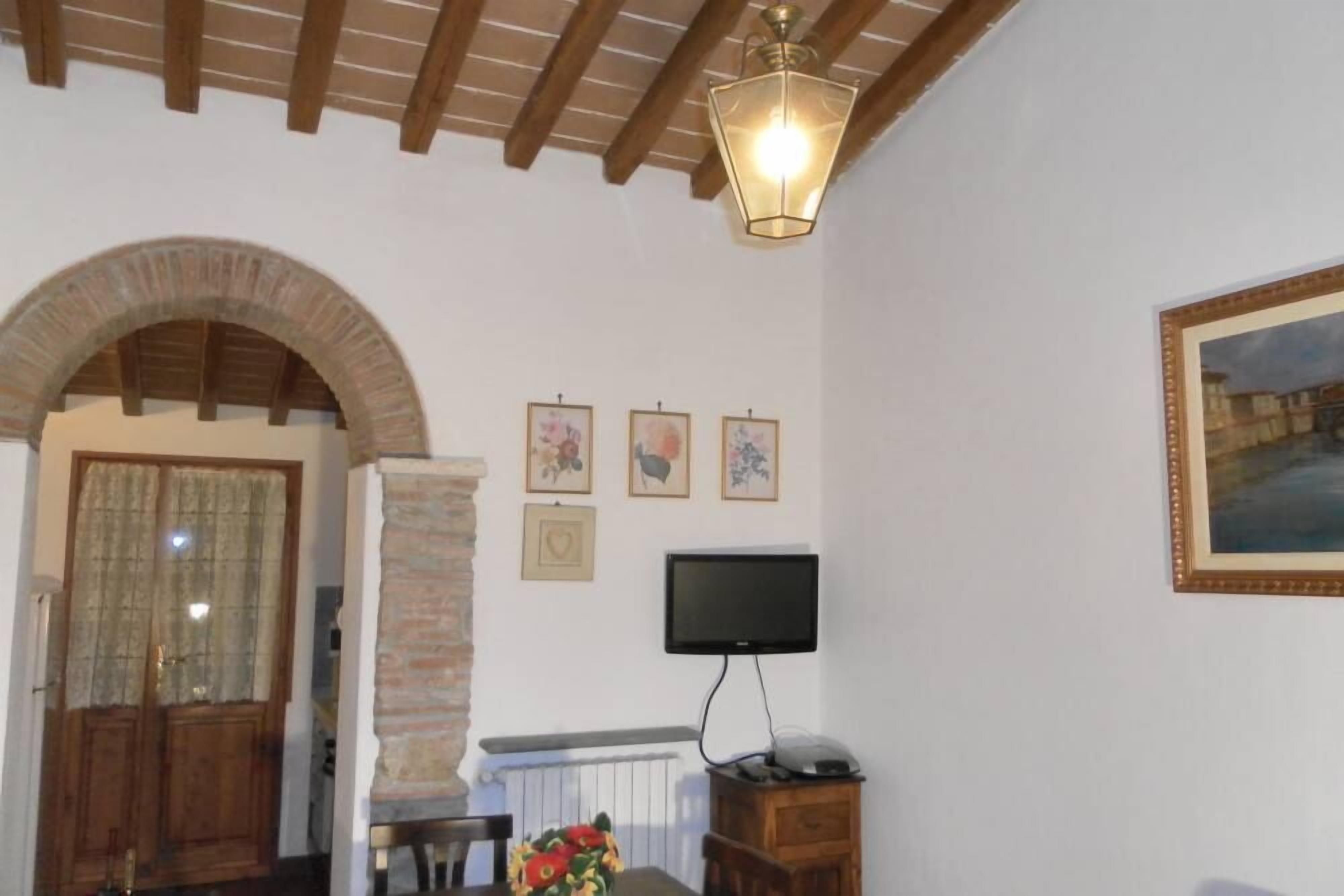 A room with a wooden ceiling, a stone pillar, a television on a wooden stand, and a framed picture on the wall.
