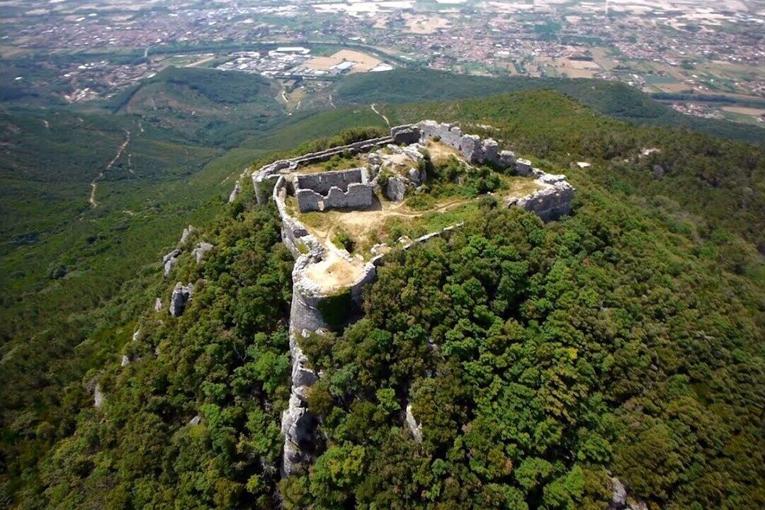 An aerial view of a historical site with ruins on a hill surrounded by dense forest.