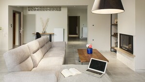 Un salon moderne avec un canapé, une table basse sur laquelle se trouvent un ordinateur portable et un livre, une cheminée et une lampe suspendue.