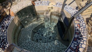 Un bain à remous en pierre, orné de mosaïques et doté de rampes métalliques.