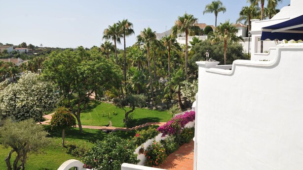 Un edificio blanco con vista a un jardín, con palmeras y plantas florecientes.