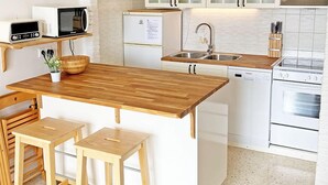 Una cocina compacta con armarios blancos, una isla de madera con taburetes, un microondas, un refrigerador, un lavavajillas y un horno.