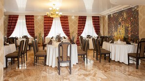 Un comedor formal con varias mesas y sillas, una araña y papel tapiz estampado.