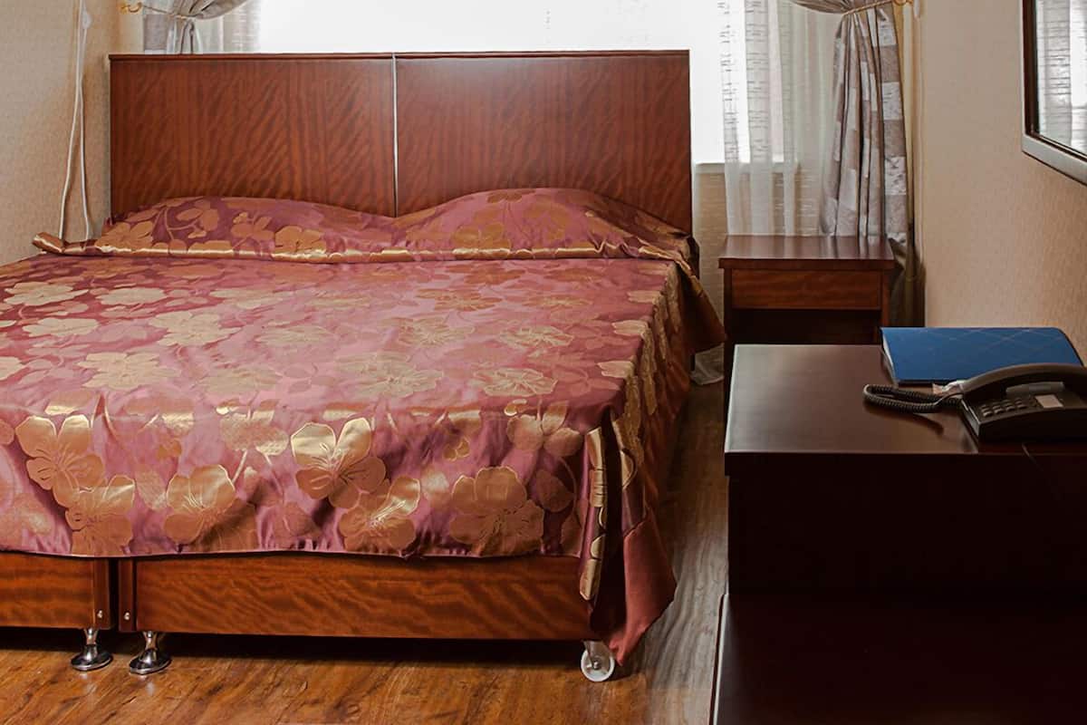 A bedroom with a wooden bed, a chandelier, a desk with a phone and a blue folder, and curtains on the windows.