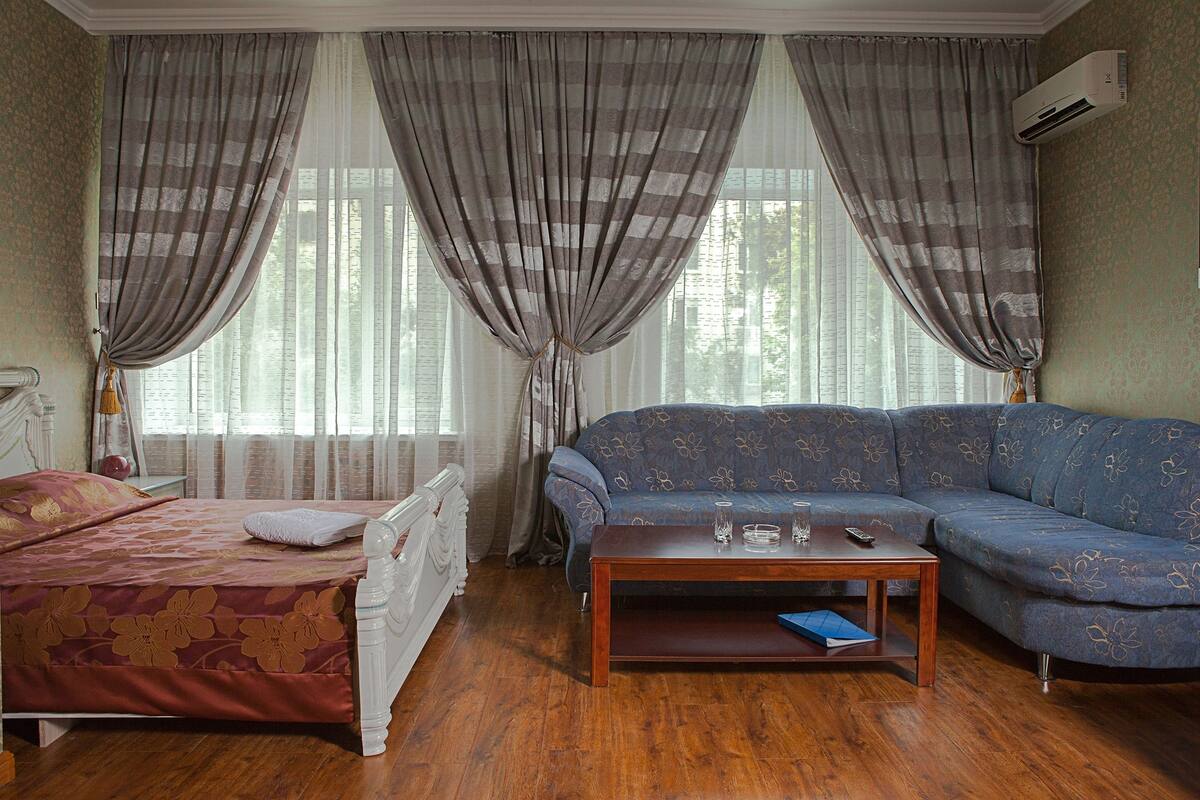 A room with a bed, a sofa, a coffee table, and a window with curtains.