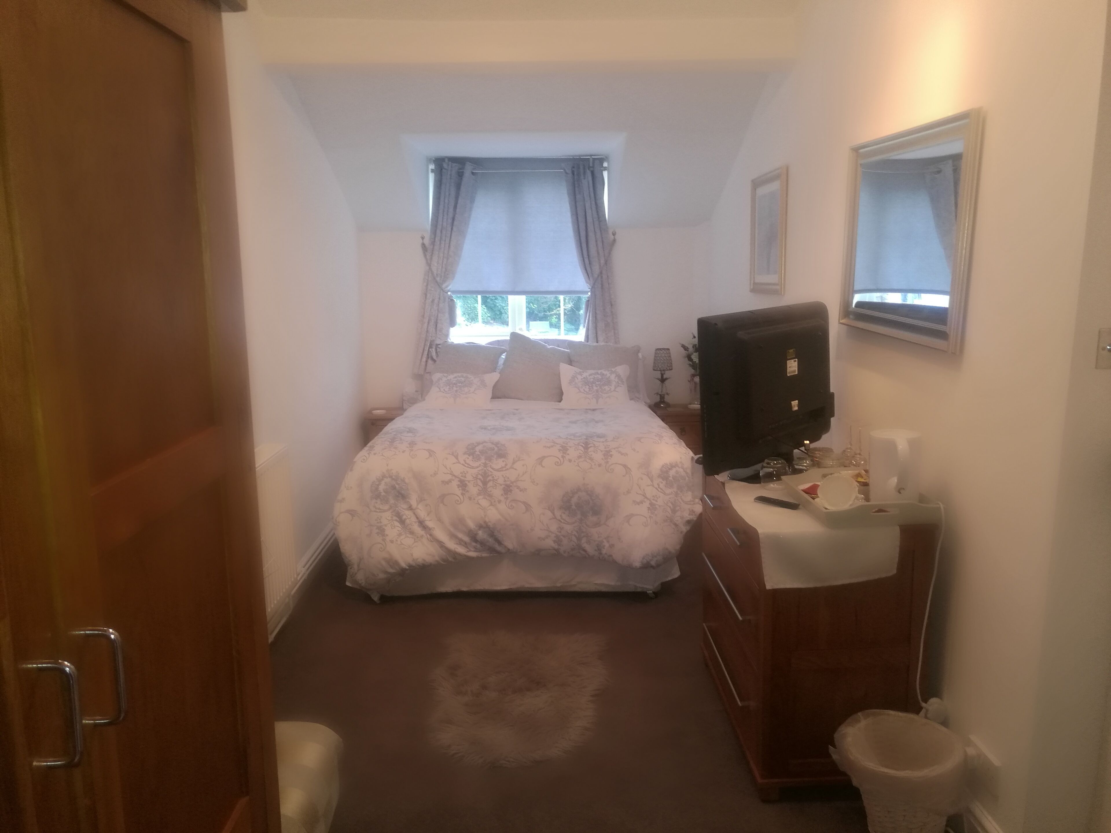 A bedroom with a bed, a TV, a dresser, and a window with curtains.