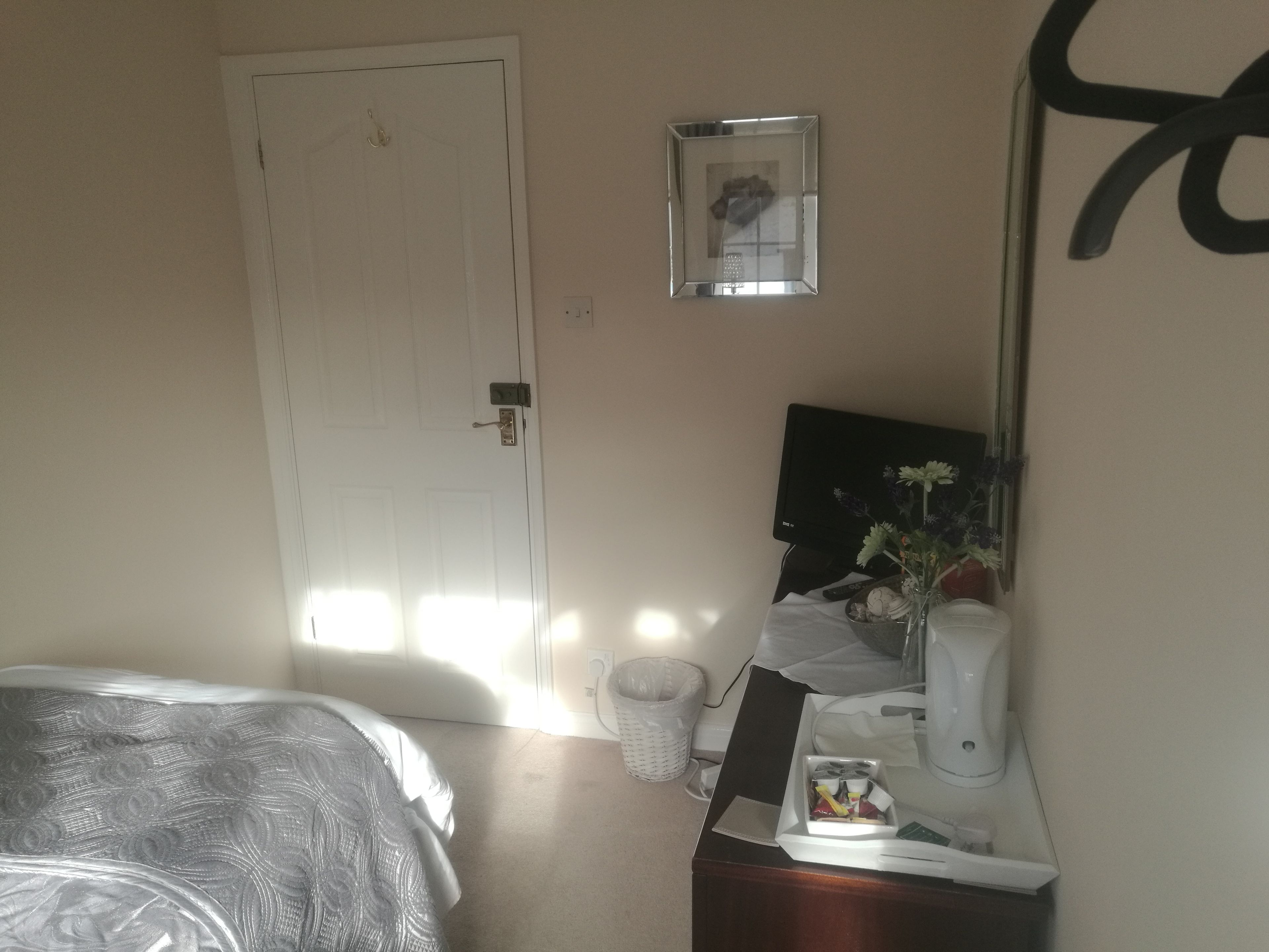 A hotel room with a bed, a desk with a computer, a coffee maker, and a mirror.