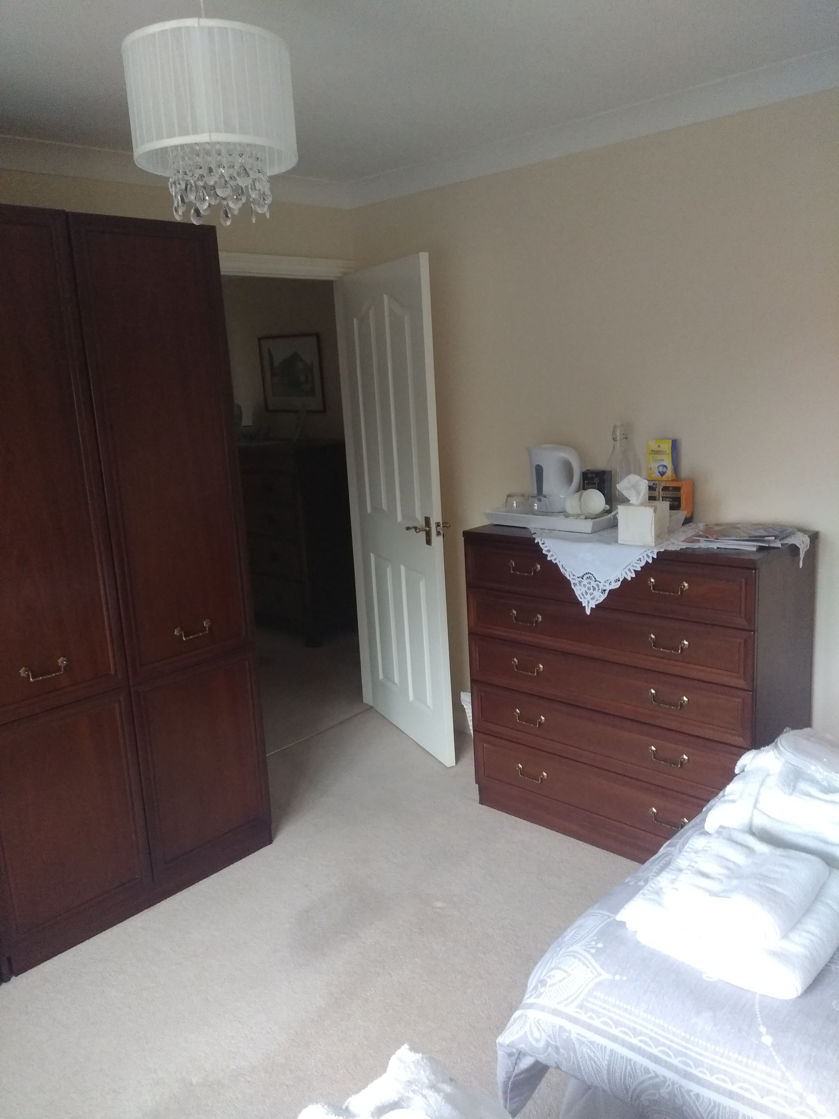 A bedroom with a wooden wardrobe, a dresser, a bed with white bedding, and a chandelier.