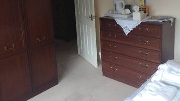 A bedroom with a wooden wardrobe, a dresser, a bed with white bedding, and a chandelier.