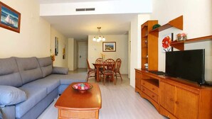 A living room with a grey sofa, a wooden coffee table, a dining table with chairs, a TV on a wooden cabinet, and artwork on the walls. - Apartment 200 meters from the beach next to the to (Denia)
