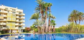 A hotel with a pool, palm trees, and a clear blue sky. - Apartment 200 meters from the beach next to the to (Denia)