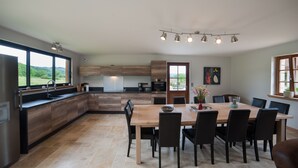 A modern kitchen with a large island, dining table, and chairs. There is a view of greenery through the windows. - Quiet new house with character, private heated pool (Sergeac)