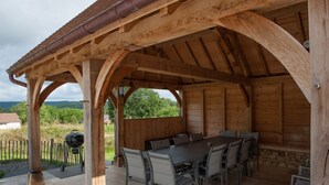 An outdoor wooden pavilion with a table and chairs, a grill, and a stone wall. - Quiet new house with character, private heated pool (Sergeac)