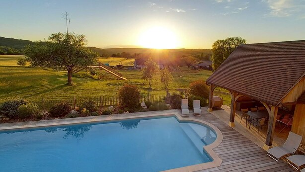 A swimming pool with a wooden deck, lounge chairs, and a wooden pavilion with outdoor seating. - Quiet new house with character, private heated pool (Sergeac)