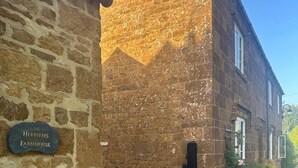 A stone farmhouse with a black gate, a brick wall, and a sign reading 'Herrieffs Farmhouse.'