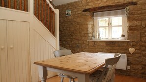 A rustic room with a wooden table, chairs, a staircase, and a stone wall.