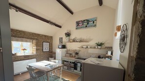 A kitchen with a dining table, chairs, a refrigerator, a microwave, and a window with flowers.