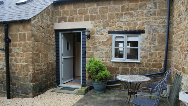 A stone building with a door, a window, a potted plant, and a small table with chairs.