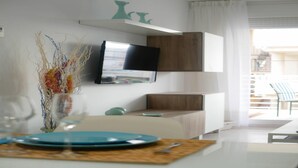 A modern living room with a flat-screen TV mounted on the wall, a dining area with a table set for two, and a view of the outside balcony. - Apartment at 20 m.de the beach with private parking bicycles (Peñíscola)
