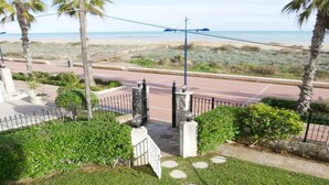 A gated entrance with a pathway leading to a road, surrounded by greenery and palm trees, overlooking a beach. - Apartment at 20 m.de the beach with private parking bicycles (Peñíscola)