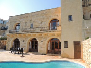 A stone building with arched windows and doors, a pool, and outdoor furniture. - Beautifully Farmhouse With Private Pool (Xaghra)