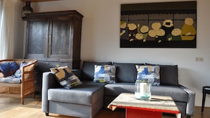 Un salon avec un canapé gris, un fauteuil en osier, un meuble en bois et un tableau accroché au mur.