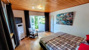 Une chambre avec un plafond en bois, un lit recouvert d’une couette à carreaux, une chaise, un bureau avec une télévision et un tableau accroché au mur.