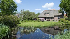 Une maison au toit de chaume, entourée d’un jardin bien entretenu et d’un étang.
