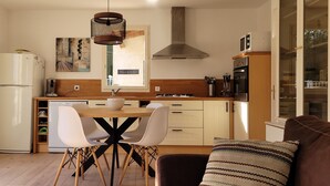 A modern kitchen with a dining area, wooden cabinets, a stainless steel range hood, and a window overlooking the outdoors. - house / villa - 3 rooms - 6 persons (Pont-Saint-Esprit)