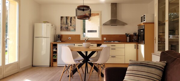Una cocina moderna con comedor, armarios de madera, extractor de acero inoxidable y ventana con vistas al exterior.