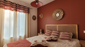 A bedroom with a bed, curtains, a wall-mounted mirror, and a woven headboard. - house / villa - 3 rooms - 6 persons (Pont-Saint-Esprit)