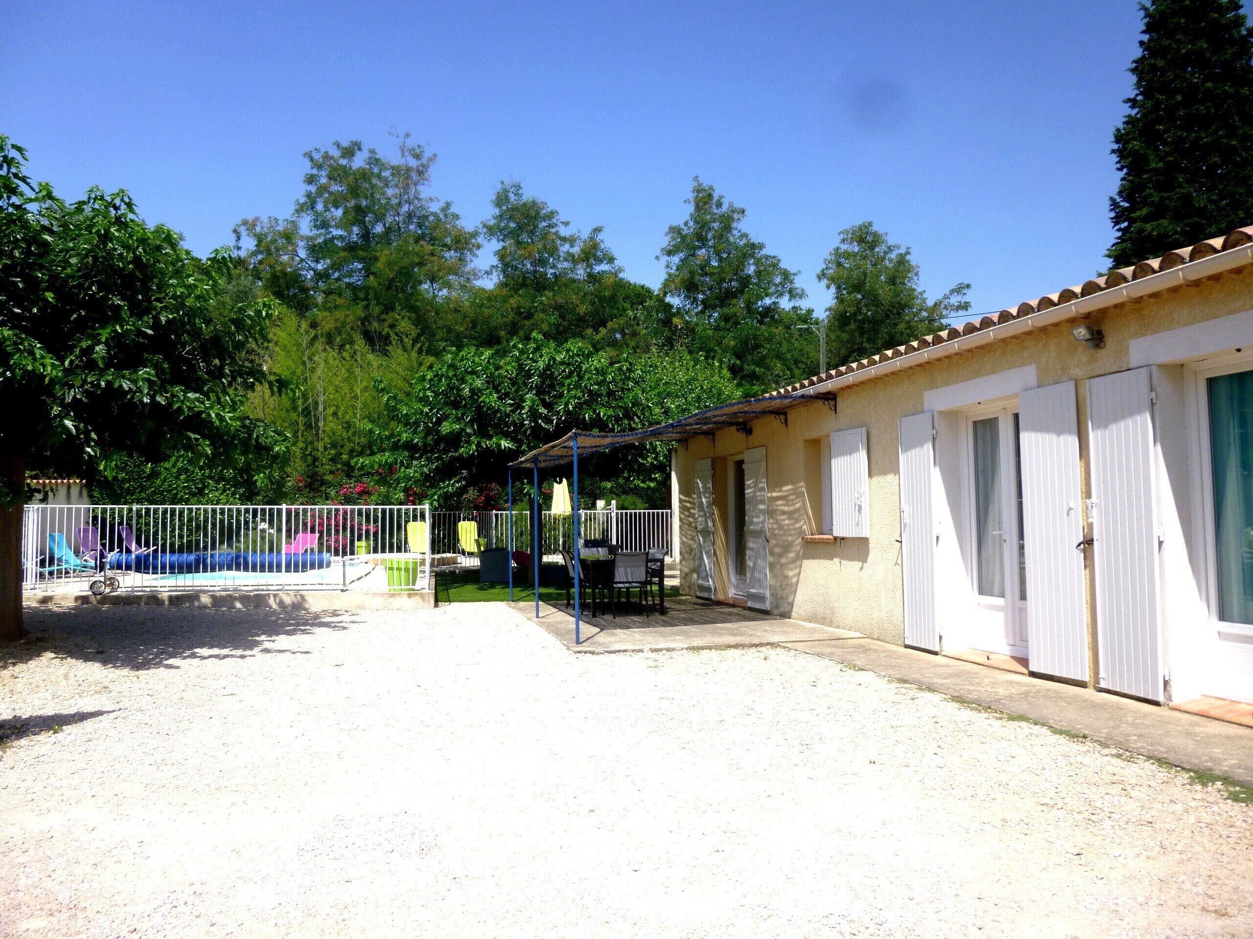 A building with a covered patio area, a fenced swimming pool, and a gravel driveway.