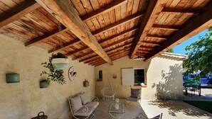 A covered patio area with wooden beams, a sofa, two chairs, a small table, and hanging plants. - house / villa - 3 rooms - 6 persons (Pont-Saint-Esprit)