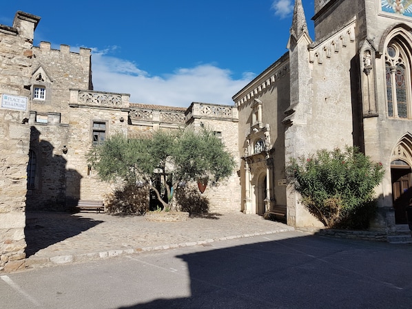 A historic stone building with a courtyard, featuring a gate, a statue, and a sign indicating a place of interest.