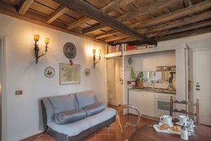 Un salon chaleureux avec un canapé, une table à manger où l’on aperçoit des croissants et des tasses de café, et une cuisine en arrière-plan.