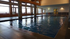 Una piscina interior amb pilars de pedra, bigues de fusta i grans finestres.