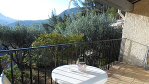 Een balkon met een witte tafel en stoelen, met uitzicht op een bergachtig landschap.