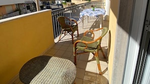 A balcony with wicker furniture, a table with a tablecloth, and a view of buildings and a street. - Otranto, very central, 50 m from the sea luxurious apartment  (Otranto)