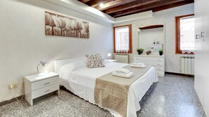 A bedroom with a bed, bedside tables, a nightstand, a mirror, and a radiator.